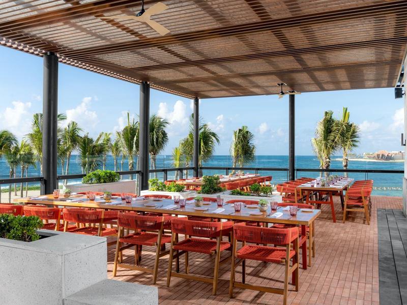 Offene Terrasse mit roten Stühlen, Holzdach und Meerblick bei klarem Himmel.