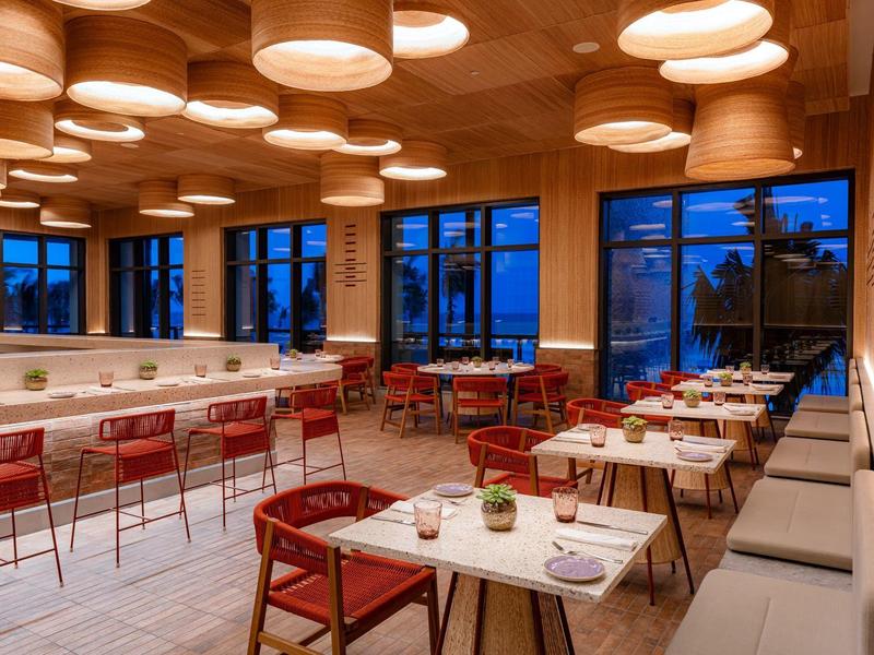 Modernes Restaurant mit warmem Holzdekor, roten Stühlen und großen Fenstern bei Dämmerung.