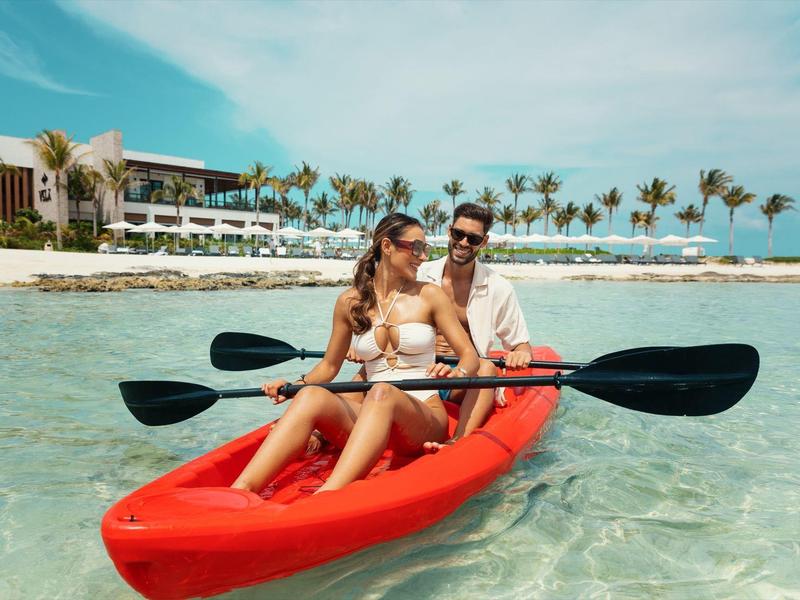 Ein Paar paddelt in einem roten Kajak auf klarem, türkisfarbenem Wasser bei sonnigem Himmel.