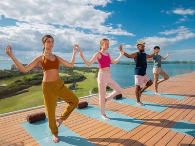 Cuatro personas practican yoga en una terraza de madera con vista al paisaje y al agua.