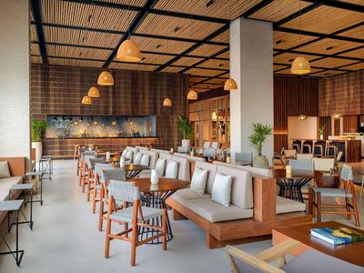 Restaurant d'hôtel moderne avec accents en bois, espaces de détente confortables et éclairage chaleureux.