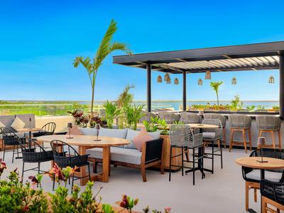Espace piscine ouvert d'hôtel avec sièges, bar et vue sur champ vert sous un ciel clair.