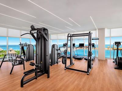 Gimnasio luminoso con equipo moderno y grandes ventanas panorámicas con vista al mar.