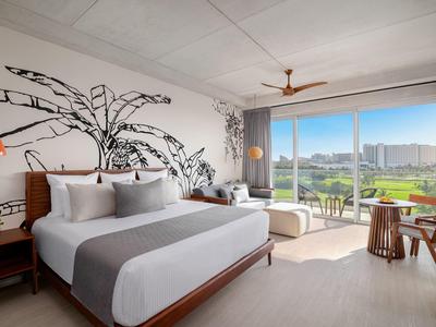 Chambre d'hôtel moderne avec grand lit, art mural et vue sur la ville à travers des fenêtres du sol au plafond.