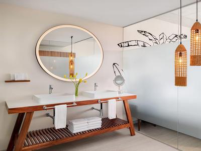 Espace salle de bain moderne avec meuble en bois, miroir rond et deux suspensions.