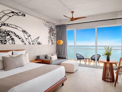 Chambre d'hôtel moderne avec vue sur la mer, lit double, coin salon et balcon avec chaises.