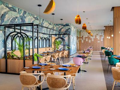 Restaurant moderne avec mur végétal, chaises colorées et éléments en bois chaleureux et éclairage.