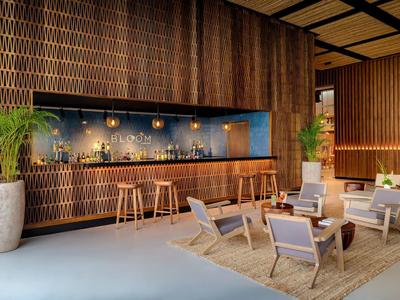 Bar d'hôtel avec boiseries, comptoir, tabourets de bar et espace salon avec fauteuils sur un tapis.