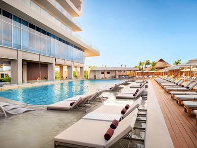 Piscine extérieure moderne avec chaises longues et parasols à côté d'un bâtiment hôtelier sous un ciel dégagé.