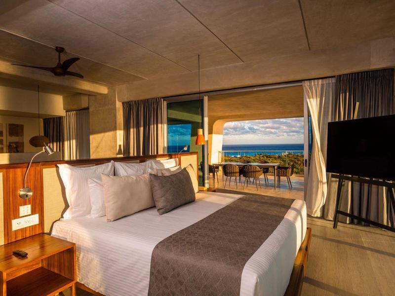 Chambre d'hôtel moderne avec lit confortable et vue sur la mer à travers de grandes fenêtres.