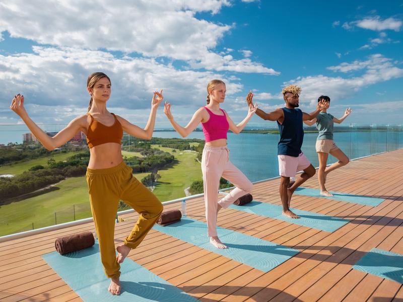 Quatre personnes pratiquent le yoga sur une terrasse avec vue sur la mer sous un ciel dégagé.