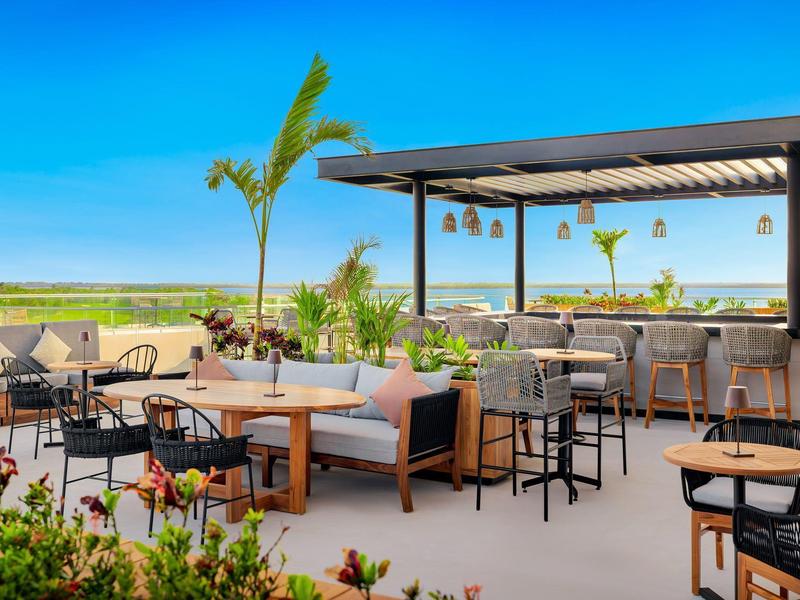 Espace piscine ouvert d'hôtel avec sièges, bar et vue sur champ vert sous un ciel clair.