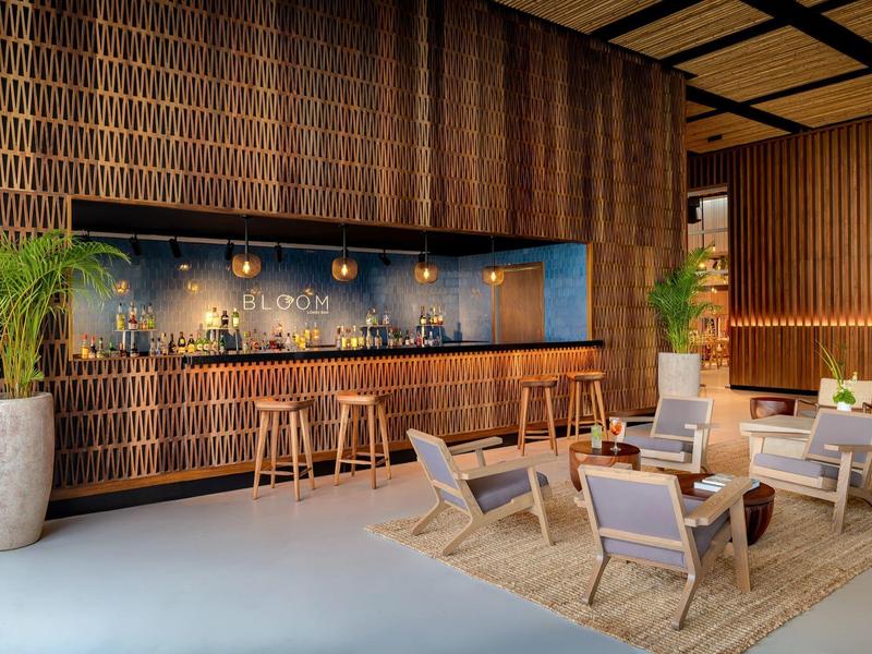 Bar d'hôtel avec boiseries, comptoir, tabourets de bar et espace salon avec fauteuils sur un tapis.