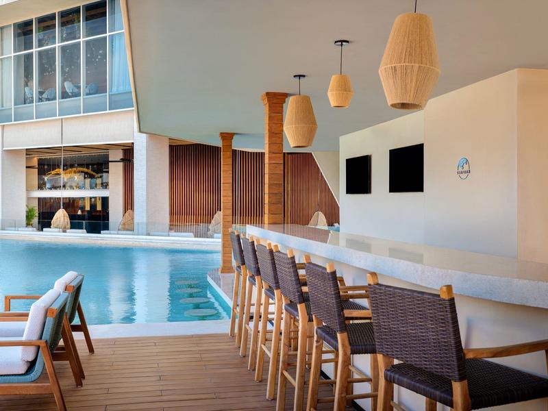 Espace piscine moderne avec bar, chaises en bois et mobilier lounge au bord de l'eau.