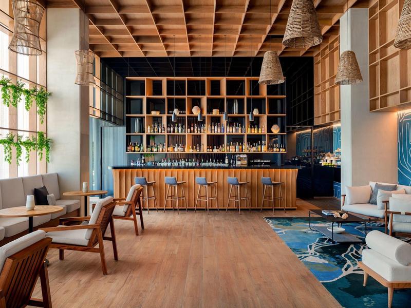 Bar d'hôtel moderne avec plafond en bois, étagères et coins salon confortables.