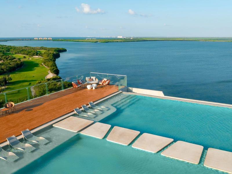 Piscine à débordement avec vue sur un grand lac et un rivage verdoyant sous un ciel clair.