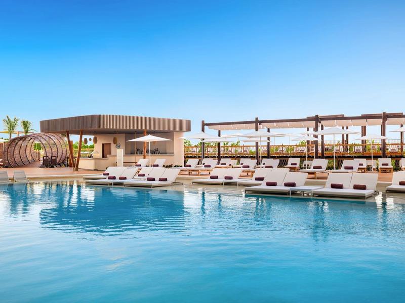 Espace piscine moderne avec transats et pavillons sous un ciel bleu clair