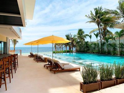 Moderner Poolbereich mit Sonnenliegen, Sonnenschirm und Bar am Meer in tropischer Umgebung.