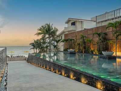 Moderner Hotelpool mit Blick auf das Meer bei Sonnenuntergang und Palmen.