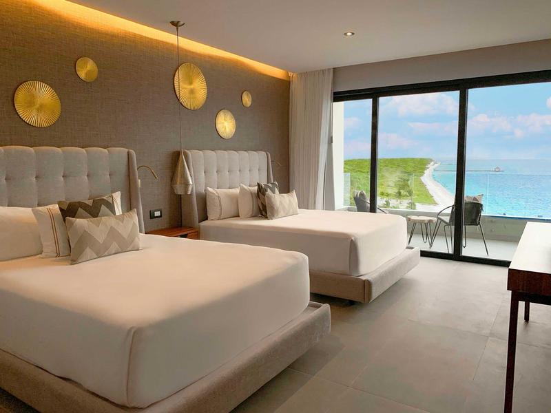 Camera d'albergo luminosa con due grandi letti e vista sul mare dalla terrazza.