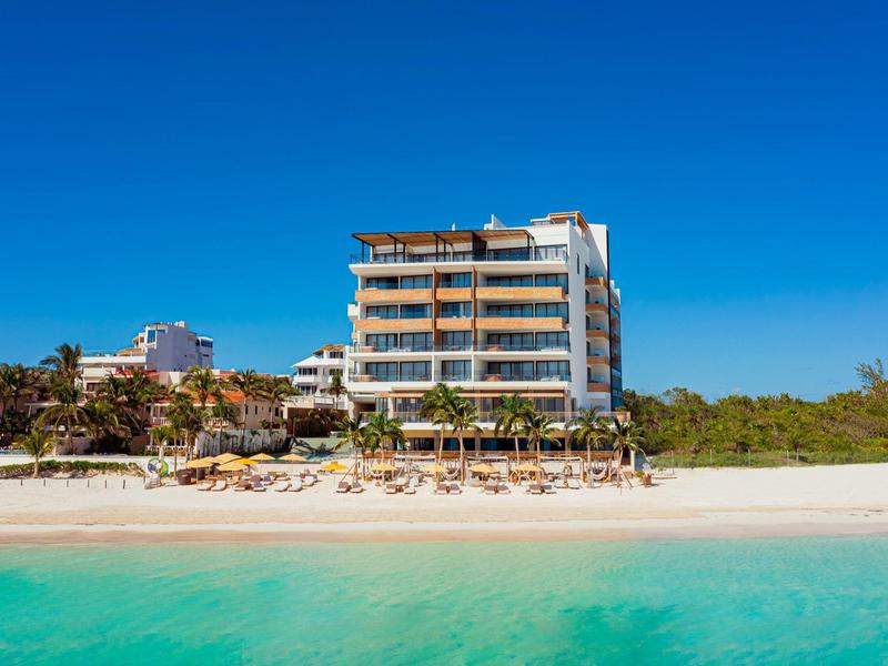 Hotel sul mare con spiaggia di sabbia bianca e acqua turchese sotto un cielo limpido.