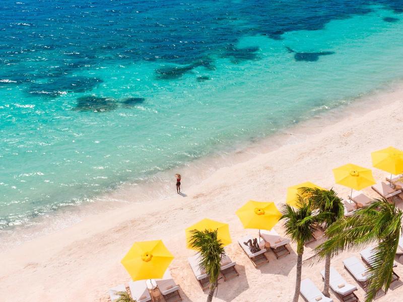 Spiaggia con ombrelloni gialli, palme e mare turchese visto dall'alto.