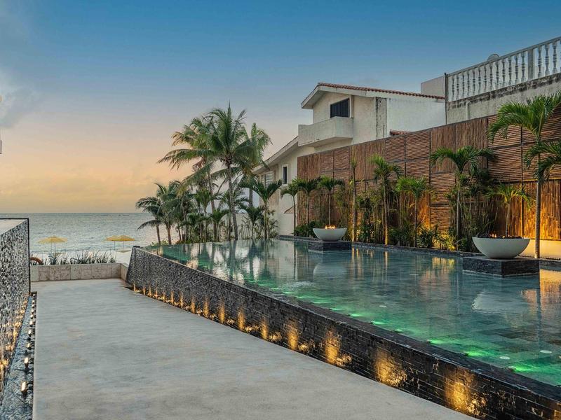 Piscina a sfioro con vista mare al tramonto, circondata da palme e luce soffusa.