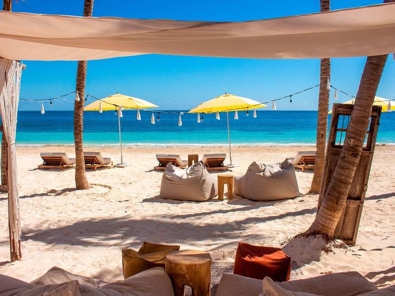 Spiaggia sabbiosa con ombrelloni gialli, sedute comode e mare blu sullo sfondo.
