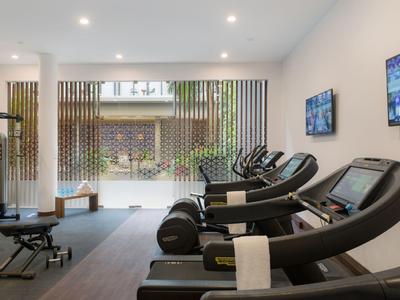 Moderní posilovna s běžeckými pásy, činkami a velkými okny s výhledem do zahrady.