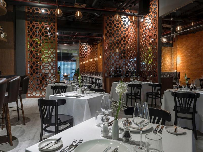 Sala ristorante con tavoli elegantemente apparecchiati e sedie nere in un ambiente moderno.