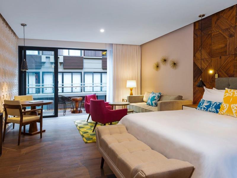 Camera d'hotel moderna con letto matrimoniale, poltrone rosse e vista sulla città.