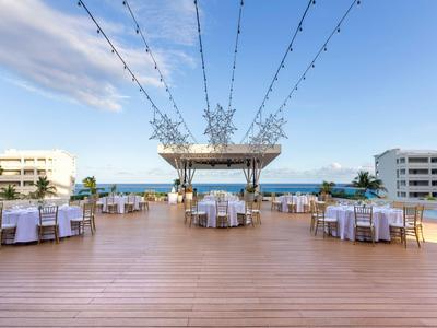 Große Terrasse mit Holzdeck, runden Tischen, Stühlen und Lichterketten unter blauem Himmel.