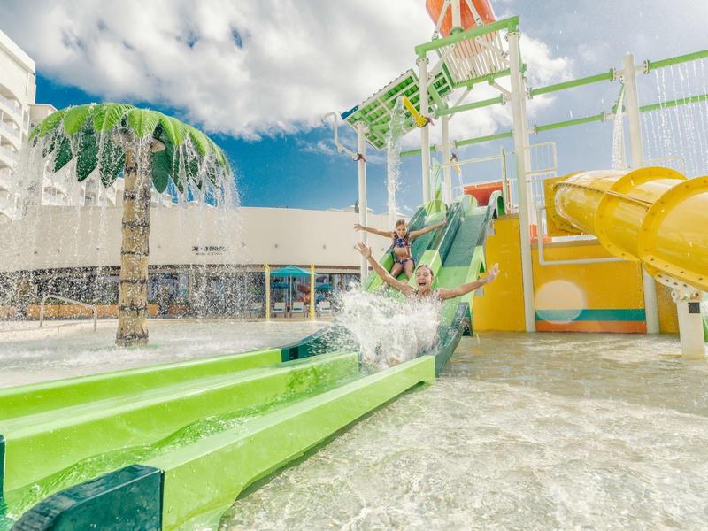 Bunte Wasserrutsche mit gelbem Tunnel, blauer Rutsche und künstlicher Palme in hellem Schwimmbad.