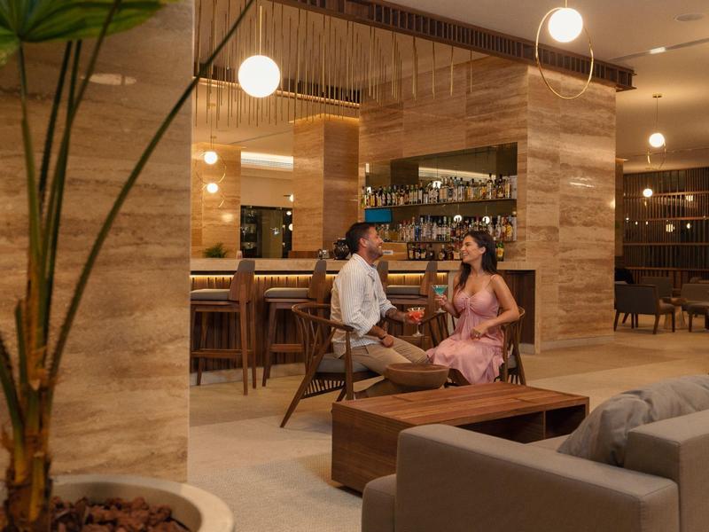 Moderner Wohnraum mit Holzvertäfelung, Sofa, Bar und Paar im Gespräch bei warmem Licht.