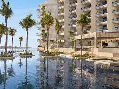 Moderner Hotelpool mit Palmen, Liegestühlen und Glasbalustraden bei klarem Himmel.
