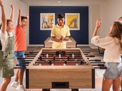 Bambini giocano a calcio balilla e festeggiano attorno a un tavolo da calcetto in una sala ricreativa.