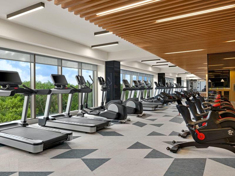 Großer Fitnessraum mit moderner Ausstattung, Laufbändern, Fahrrädern und großflächigen Fenstern.