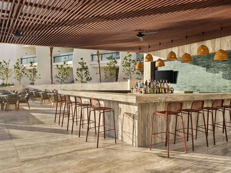 Moderner, heller Außenbereich mit großer Steintheke, hohen Holzstühlen und grünen Pflanzen.