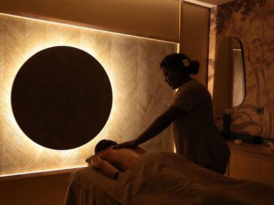 Słabo oświetlony pokój z łóżkiem do masażu, na którym ktoś jest leczony.