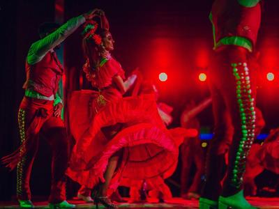Ballerini con abiti rosso acceso eseguono una performance dinamica su un palco illuminato di rosso.