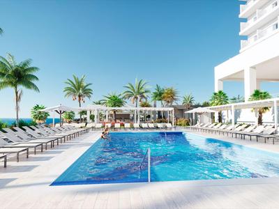 Piscina moderna dell'hotel con lettini e palme sotto un cielo blu limpido.