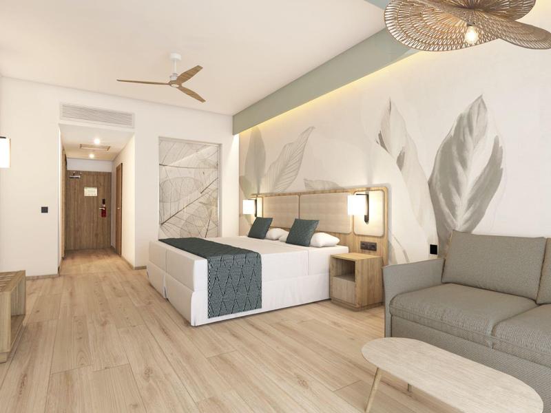 Nowoczesny pokój hotelowy z podwójnym łóżkiem, szarą sofą i jasną drewnianą podłogą