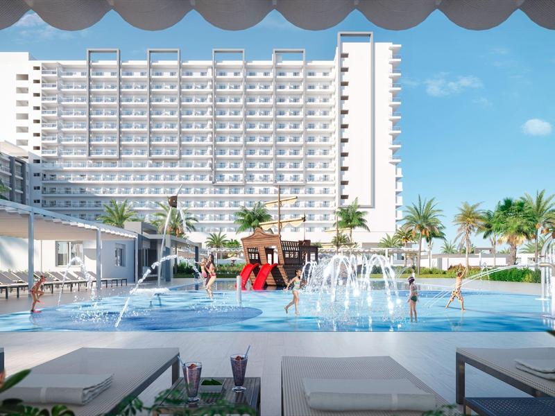 Duży basen na zewnątrz z fontannami przed nowoczesnym budynkiem hotelu w słoneczny dzień.