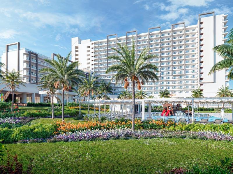 Duży hotel wielopiętrowy otoczony palmami i zadbanym ogrodem.