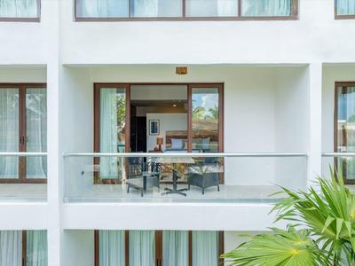 Balkon s proskleným zábradlím a stolem se židlemi u bílého hotelového objektu s rostlinami