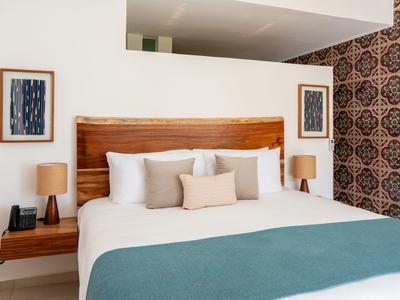 Ložnice s velkým dřevěným čelem postele, bílým povlečením a tyrkysovou přikrývkou.