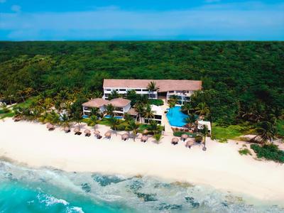 Hotel s bazénem na pláži, obklopený hustou zelení a modrou oblohou.