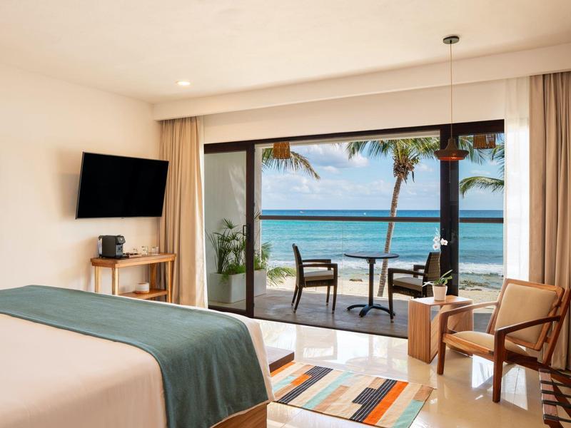 Hotelový pokoj s výhledem na moře, balkonem, dvěma židlemi, postelí a televizí.