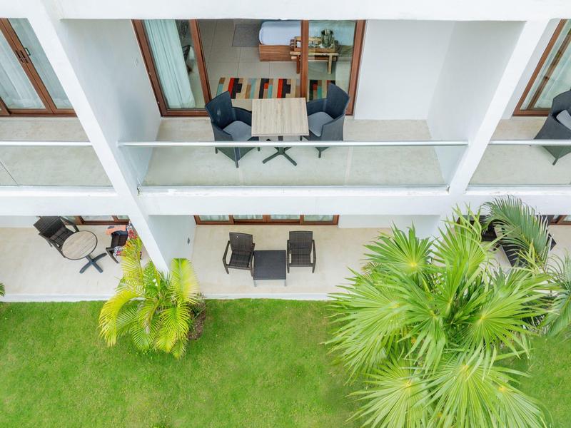 Balkony s posezením a stolem nad trávníkem s palmami před hotelem.