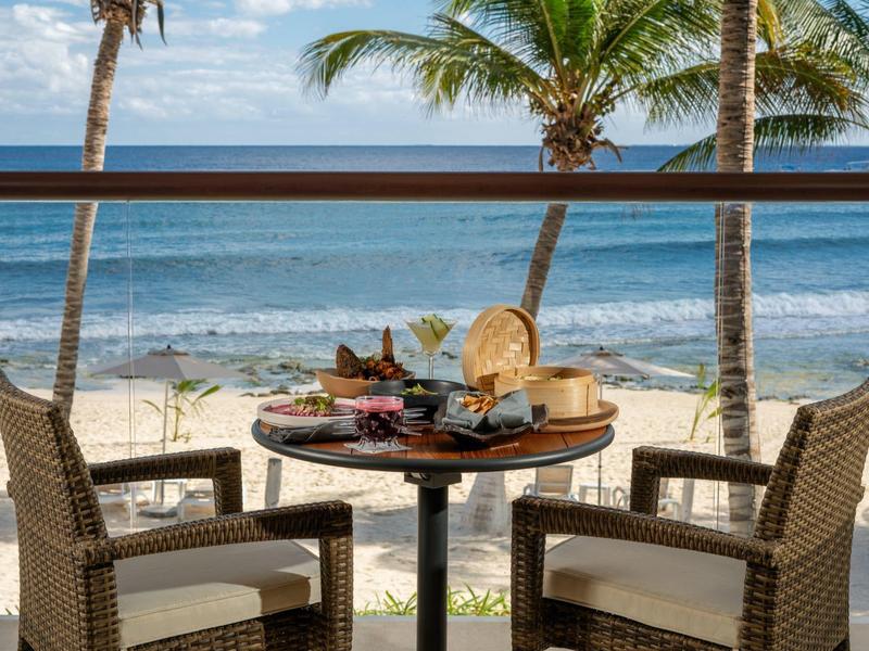 Dva židle a stůl s jídlem na terase s výhledem na pláž a moře.